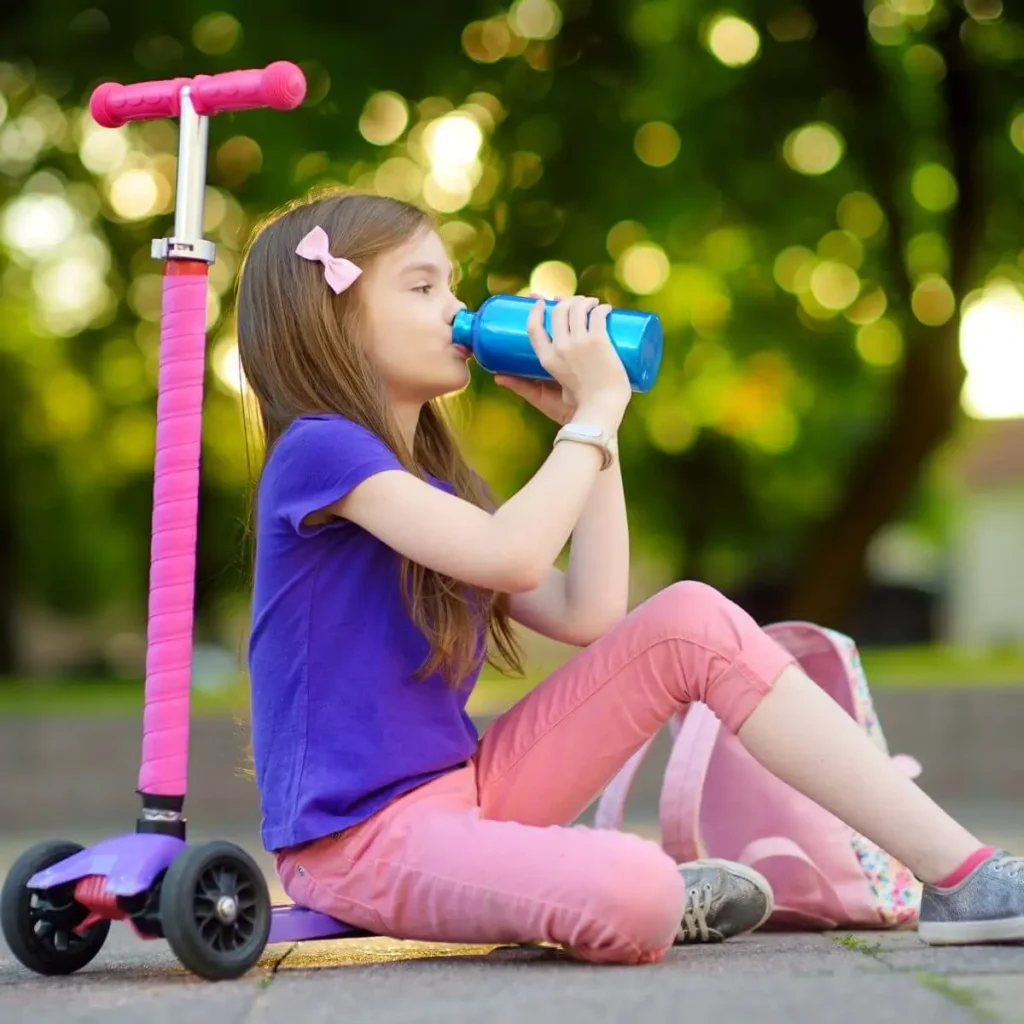 A girl drinking water sitting on a pro scooter on the street, Kick scooter exercise benefits for kids