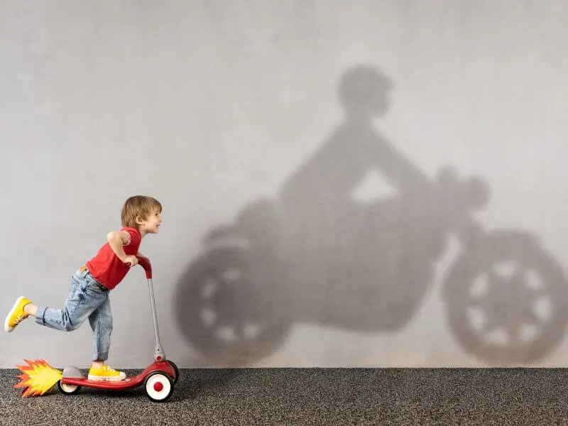 A kid on a three wheel scooter imagining as a bike rider when adult