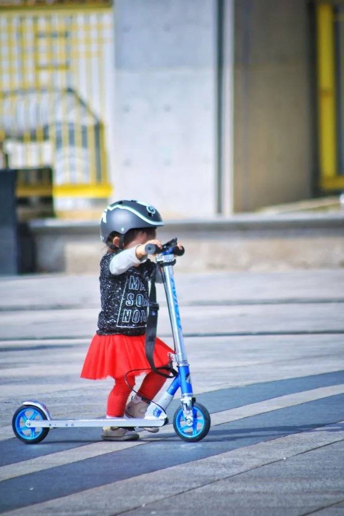 A girl wearing black helmet and black and red dress while riding a scooter. A proper electric scooter protective gear.