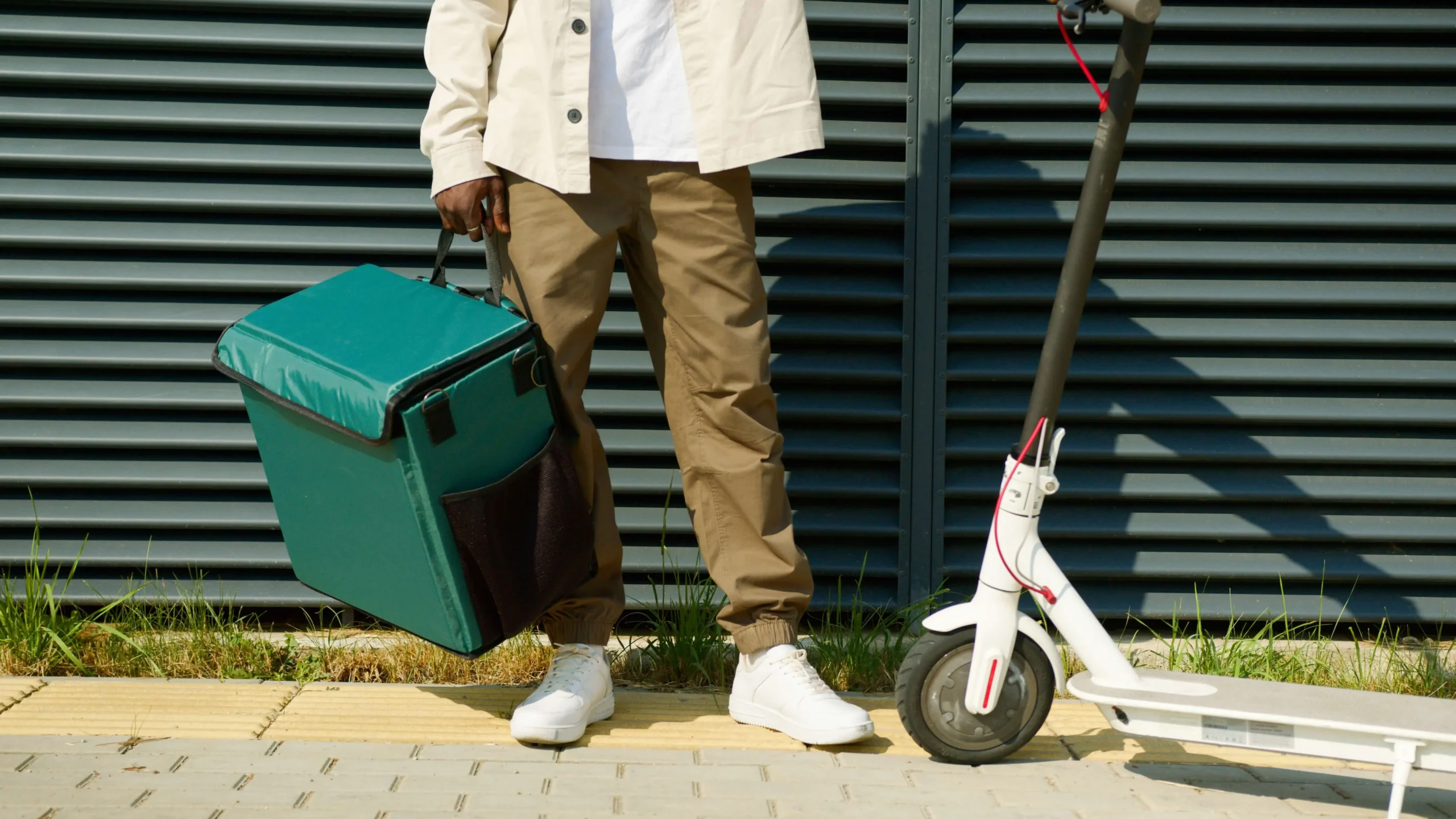 a white custom pro scooter alongside a man wearing white shirt ,brown pant and holding a green bag
