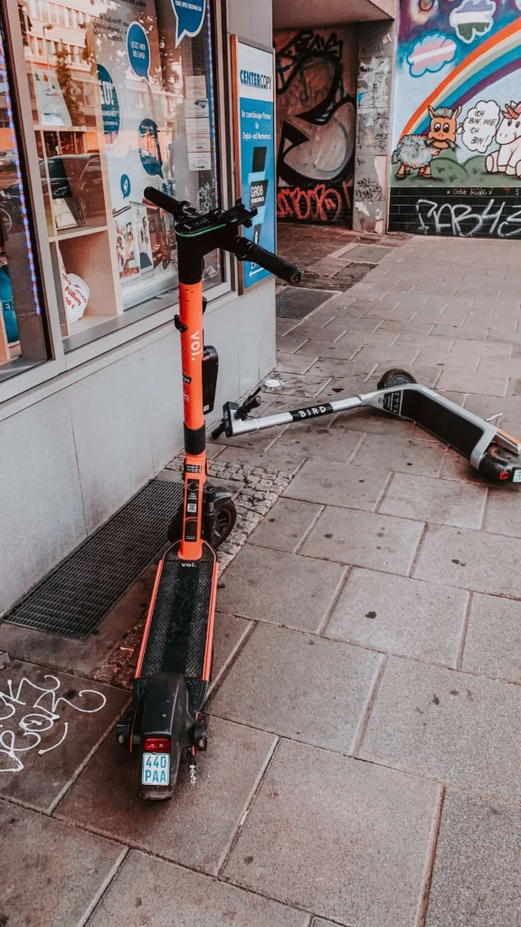Pro scooters parked outside a shop, a red scooter standing, and a grey scooter fell down