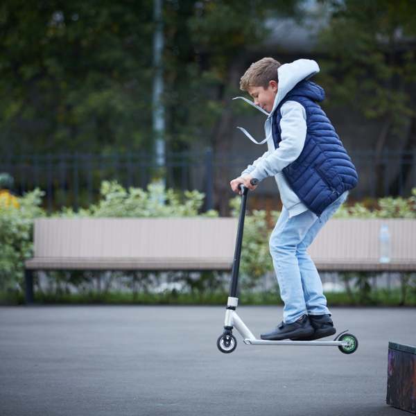 A boy doing the Bunny hop trick on a stunt scooter in  a park, easiest beginner scooter trick