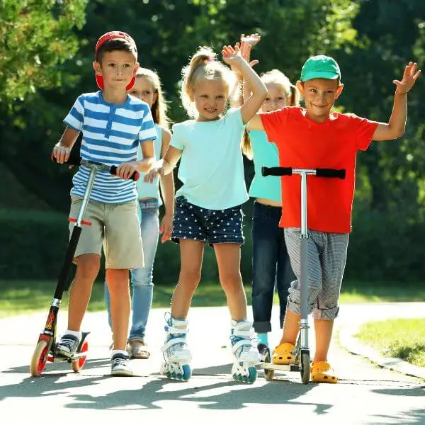five kids in a park with 2 boys on pro scooters and one girl on skates, getting the kick scooter exercise benefits.