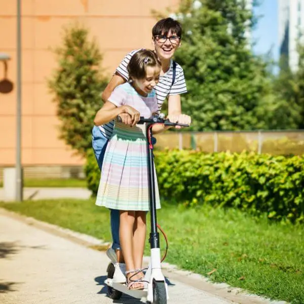 A mother encouraging  and praising her child learn to scooter