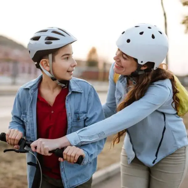 Mother and son wearing helmet while learning how to ride a scooter