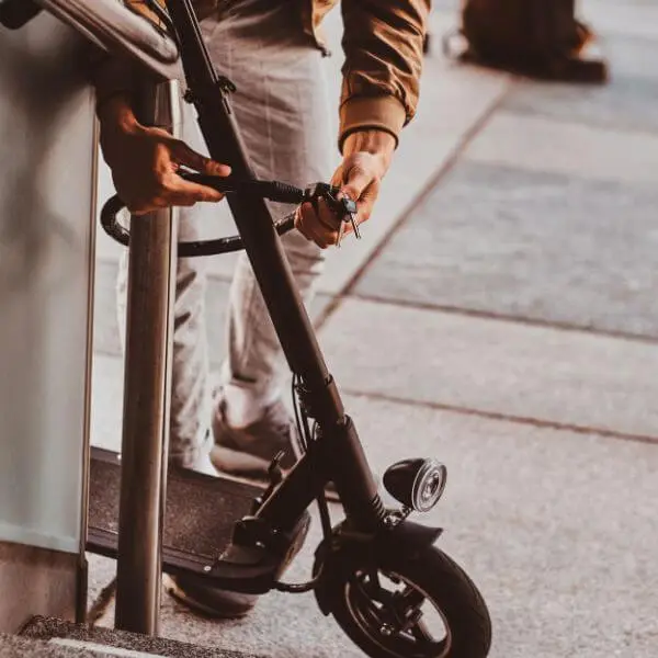 A man locking his scooter with cable lock,
telling how to lock an electric scooter